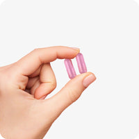 Conceive Plus Couples Bundle Fertility Support | His/Her Deal close-up of two pink Women’s Fertility Support capsules held between thumb and forefinger, illustrating capsule size and feminine design against a white background.