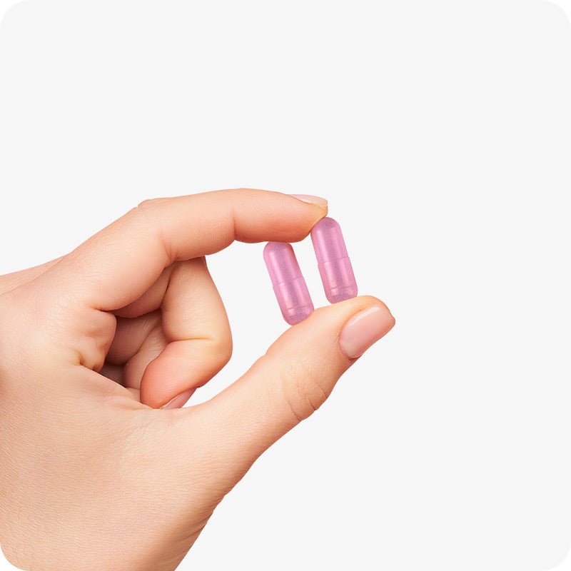 Conceive Plus Couples Bundle Fertility Support | His/Her Deal close-up of two pink Women’s Fertility Support capsules held between thumb and forefinger, illustrating capsule size and feminine design against a white background.
