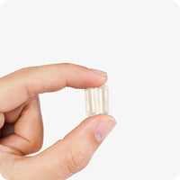 Hand holding two Conceive Plus Motility Support capsules against a white background. Beige vegan capsules are shown close-up to highlight their size and smooth texture.